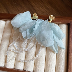 Dettaglio ravvicinato di orecchini a fiore in tulle verde menta con cuori dorati e nappe di perline