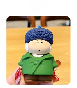 Detail of cute doll keychain with blue curly hair and green coat on a wooden table