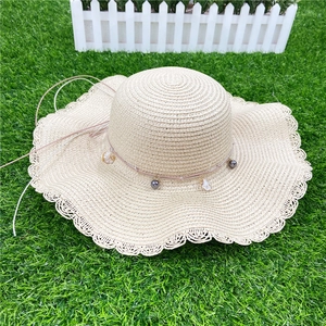 Détail d'un chapeau de paille à large bord avec perles grises et pendentifs coquillages