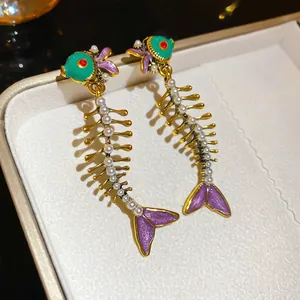 Unique fishbone drop earrings with green enamel and pearls on a white jewelry display
