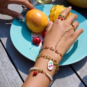 Gold cherry finger bracelet and strawberry pearl jewelry set worn in a summer scene