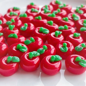 Macro detail of glossy red resin mini apple charms with green leaves for DIY crafts