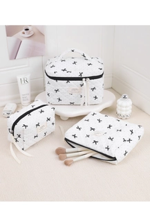Three-piece white quilted makeup bag set featuring elegant black bow prints and soft ribbon pulls