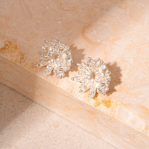 Macro di orecchini a fiore in argento con zirconi e perle su superficie in pietra