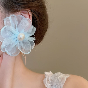 Close-up of model wearing light blue chiffon flower earrings with white faux pearl centers