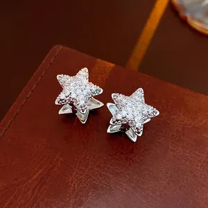 Sparkling silver star earrings with pavé zircon stones on deep brown leather background