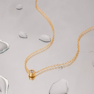 Minimalist gold titanium steel necklace with zircon pendant on reflective water surface