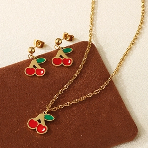 Dettaglio del set di gioielli a ciliegia dorata con collana e orecchini in smalto su camoscio