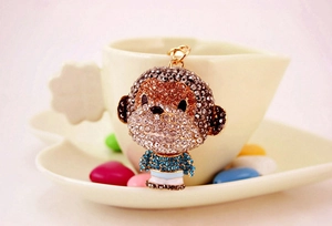 Detail of a sparkling rhinestone monkey keychain placed on a white heart-shaped saucer