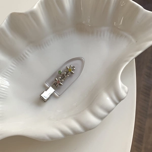 Barrette fleurie en métal avec strass colorés posée sur un plateau en forme de coquille