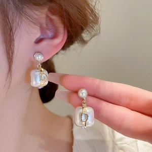 Detail view of pearl earrings with golden metal frames and a signature D letter charm