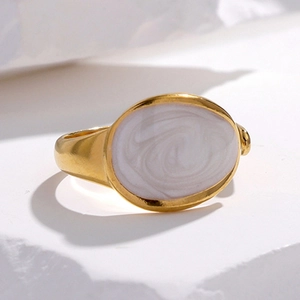 Gold oval signet ring with white marble inlay on stone background minimalist style