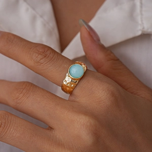 Gros plan détaillé d'une bague dorée martelée avec pierre turquoise portée à la main