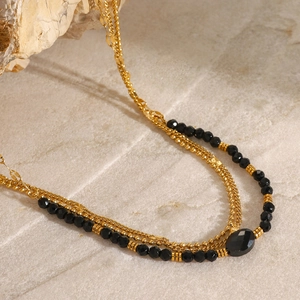 Layered gold chain necklace with black faceted beads and oval stone on stone surface