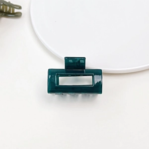 Close-up of a small rectangular dark green jelly texture hair claw clip on a white plate