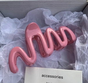 Close-up of pink wave-shaped hair claw clip with glossy finish in aesthetic packaging