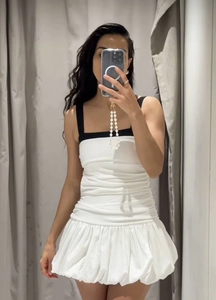 Close-up of a white puff hem dress featuring black wide straps and a pleated bodice texture