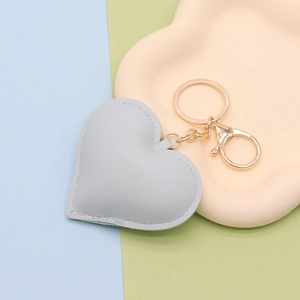 Close-up of grey heart-shaped PU leather keychain with gold metal lobster clasp and stitching
