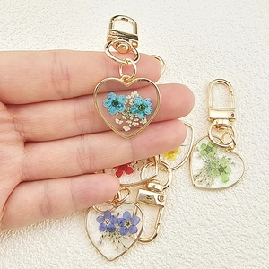 Handheld view of a heart-shaped resin keychain featuring colorful real dried flowers