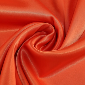 Close-up of bright orange satin fabric showing glossy texture and elegant drapes