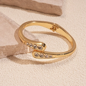 Detail eines goldfarbenen Armreifs mit runden Zirkonia auf einem strukturierten Stein