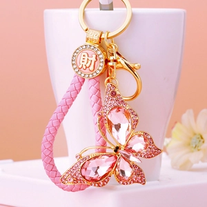 Close-up of pink crystal butterfly keychain with golden ring and woven strap detail