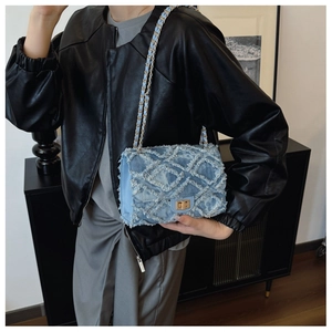 Detail of blue denim crossbody bag with quilted texture and gold chain strap