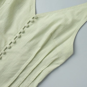 Detail of light green cotton vest with V-neck, covered buttons and pleated texture
