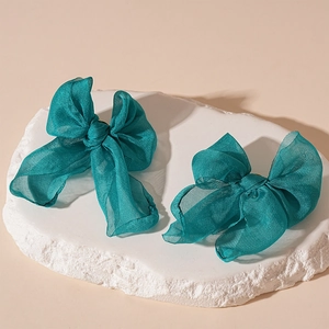 Detail view of two dark green organza bow hair clips on a minimalist stone base