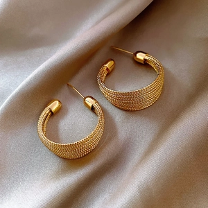 Close-up of golden mesh woven C-shape hoop earrings on elegant champagne silk fabric