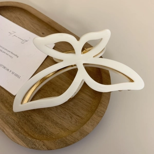 Macro detail of white butterfly claw clip with gold metal spring on a wooden tray