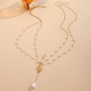 Detailed close-up of a layered gold body chain with baroque pearls and conch pendant