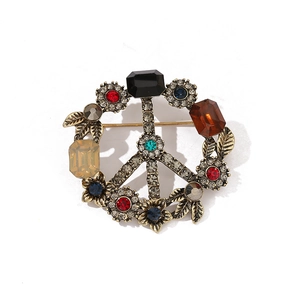 Vintage bronze peace sign brooch with colorful rhinestones and leaf motifs on white background