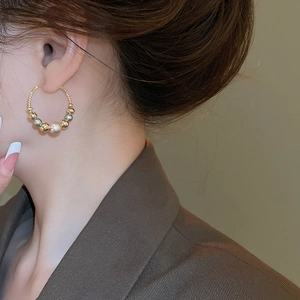 Close-up of golden twisted rope hoop earring with mixed beads and large pearl on model