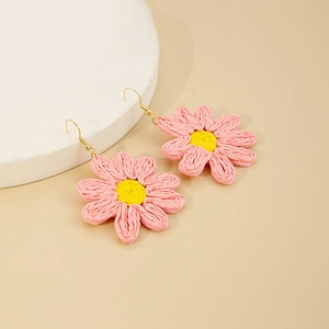Vue détaillée des boucles d'oreilles marguerites tissées main en rose avec cœur jaune