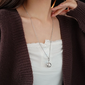 Close-up of minimalist silver spherical pendant on a fine chain worn over a brown cardigan