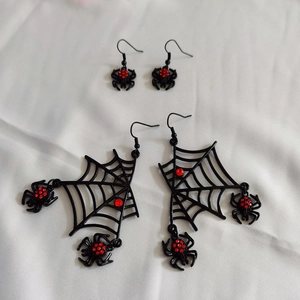 Detail of gothic spider web earrings with red rhinestones on white fabric background