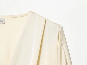 Détail du décolleté en V et des plis d'une blouse en satin couleur champagne