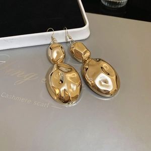 Detail of large gold liquid metal earrings featuring irregular oval shapes and hammered texture