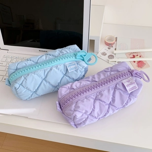 Quilted pastel blue and purple pencil cases with chunky zippers on a white desk setup