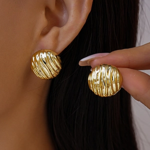 Détails des boucles d'oreilles dorées rondes avec une finition métallique texturée sur modèle