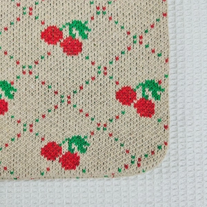 Close-up of knit cherry pattern and textured diamond grid on the beige tote bag
