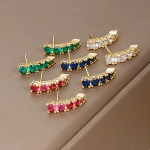 Minimalist gold stud earrings set with colorful gemstones on a brown jewelry box display