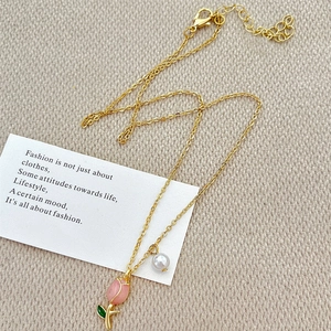 Close-up of golden necklace featuring a pink tulip pendant and white pearl charm