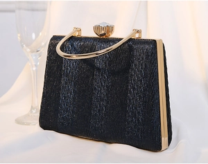 Macro view of black pleated fabric clutch with gold metal handle and large rhinestone