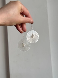 Detail of round shell pendant earrings with white beads and silver chain on hand