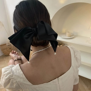 Detail of elegant large black satin bow hair clip with pearl pendant on low bun hairstyle