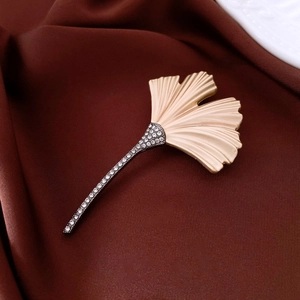 Detailed close-up of a 18k gold-plated ginkgo leaf brooch with crystals on brown satin