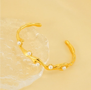 Close-up of golden 18K gold-plated bangle with wavy texture and white pearls
