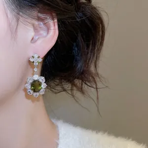 Silver flower drop earrings with oval green gemstone and zircon petals on a model